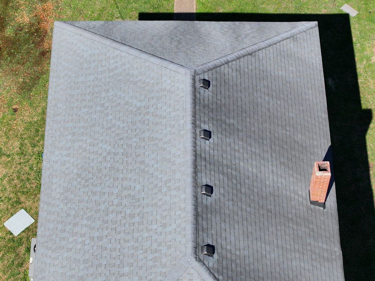 Overhead aerial view of a residential shingle roof with ridge vents and a brick chimney